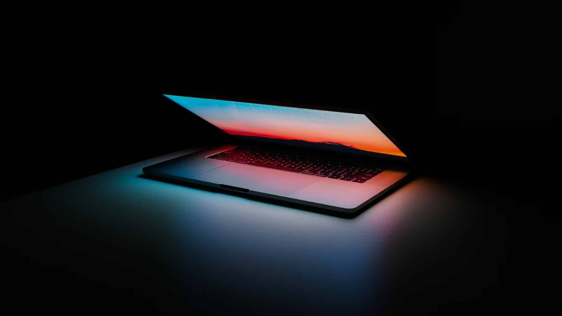 Apple macbook pro slightly open with rainbow screensaver and black background